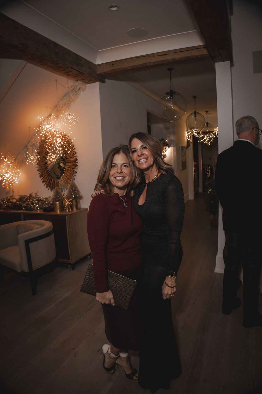 Two women smiling and posing together at an elegant evening event with warm decorative lighting.