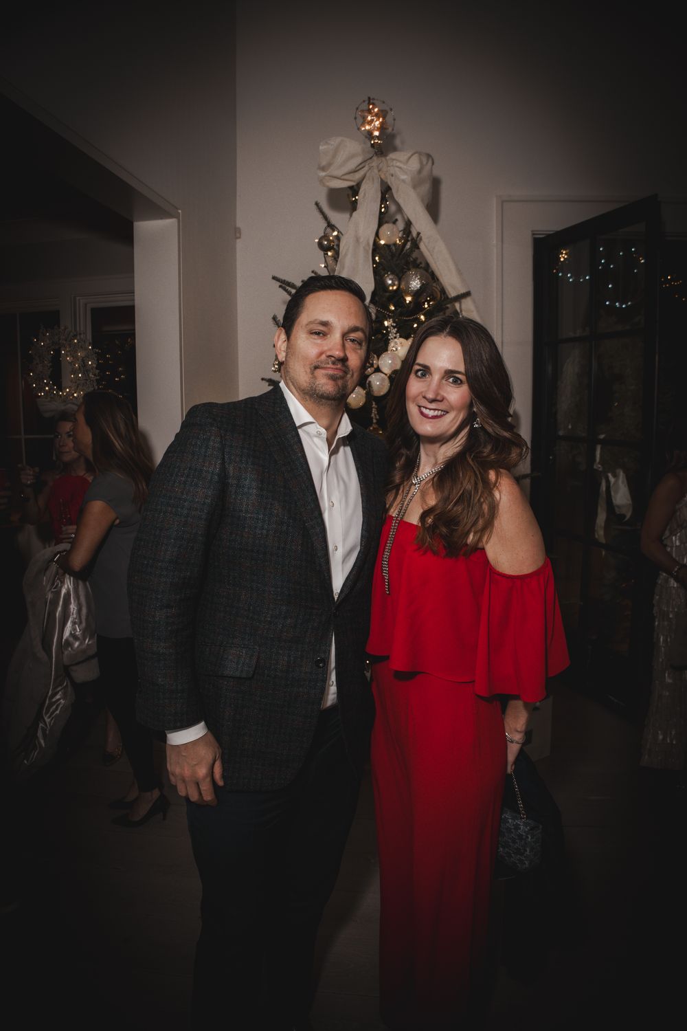 Couple posing together at a Christmas holiday party, man in suit and woman in red off-shoulder dress.
