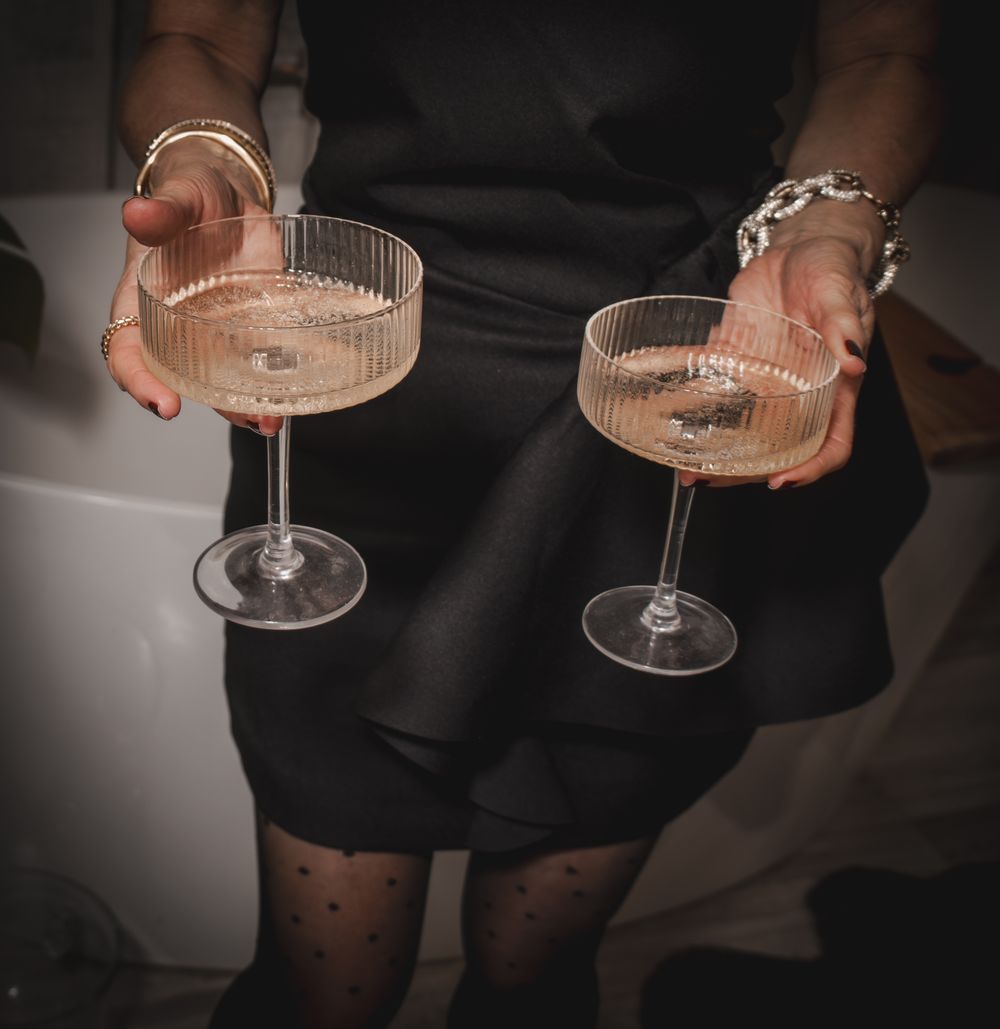 Woman in black dress holding two elegant ribbed coupe champagne glasses at a sophisticated evening event.