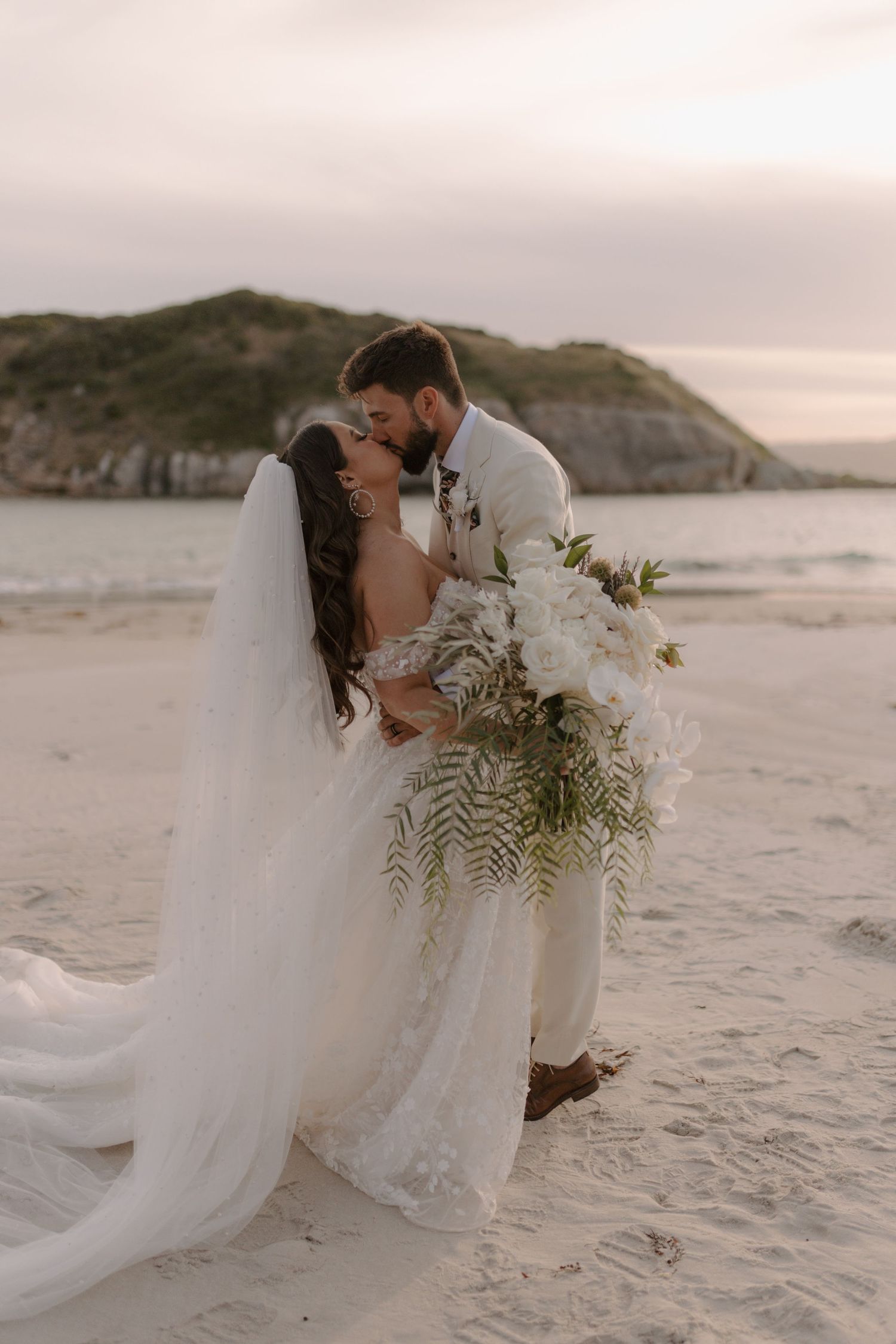 Wedding party walking down outdoor path in white attire during golden hour.