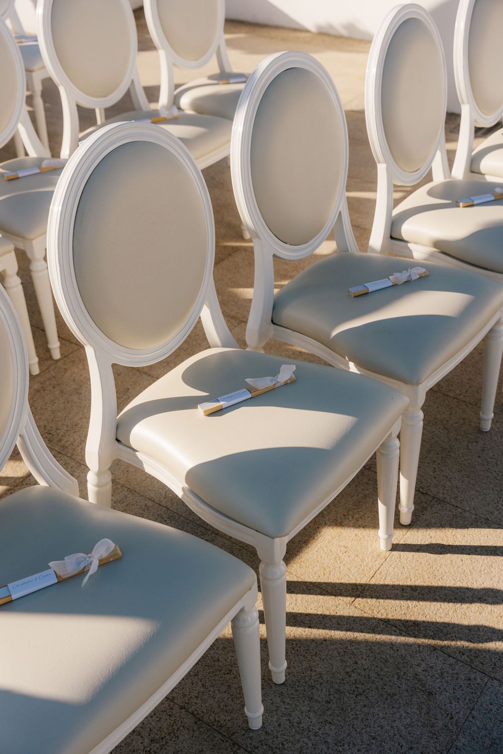 Elegant white Louis ghost chairs with oval backs arranged in rows for an outdoor wedding ceremony.