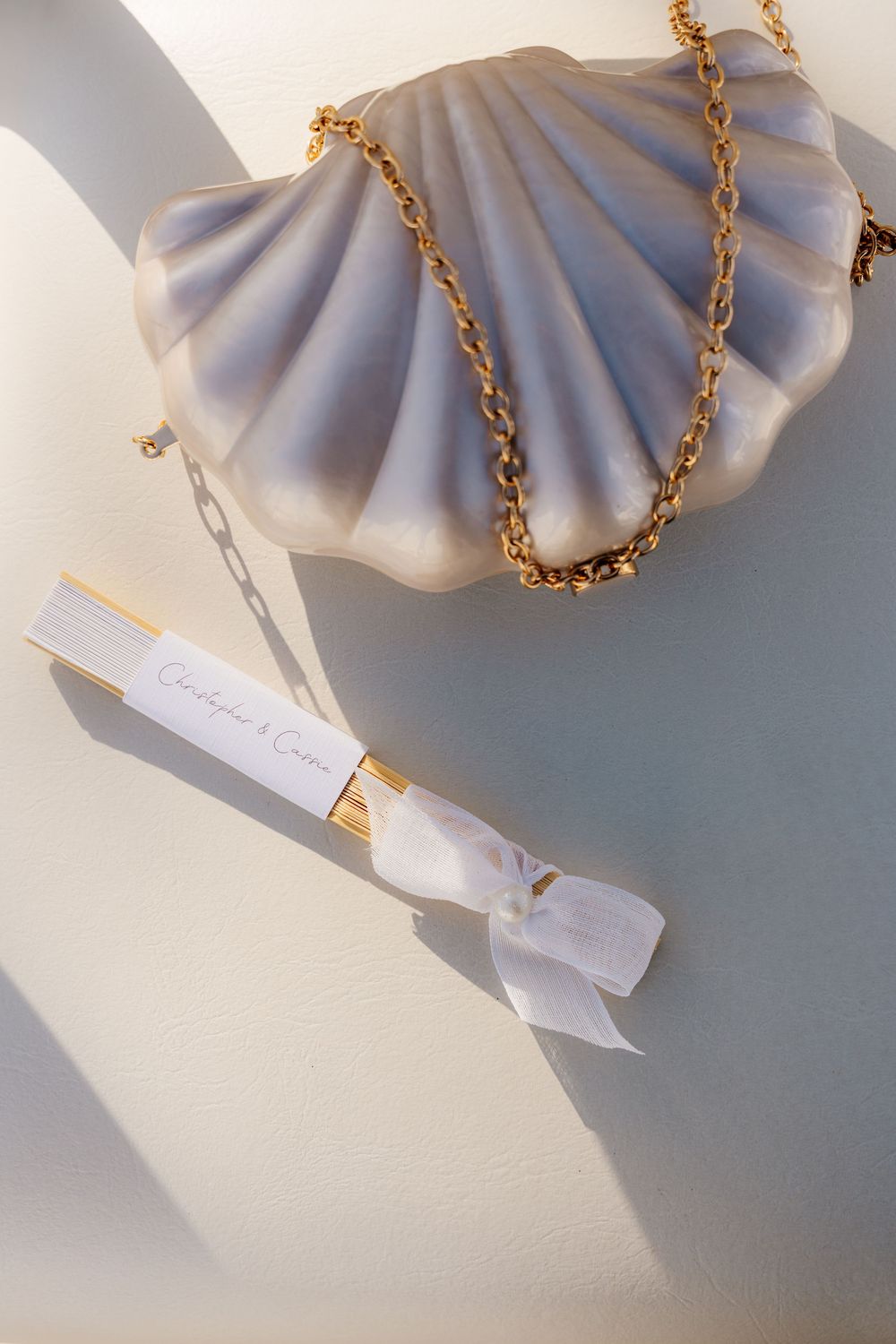 Elegant seashell clutch bag with gold chain strap beside a scroll wedding invitation tied with white ribbon.