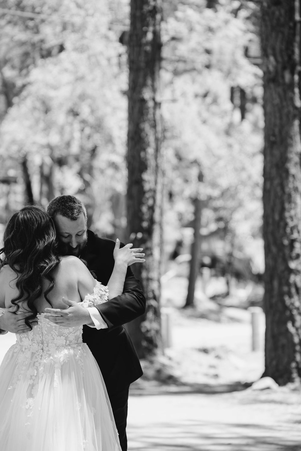 Black and white photo of bride and groom embracing tenderly among tall trees on their wedding day.