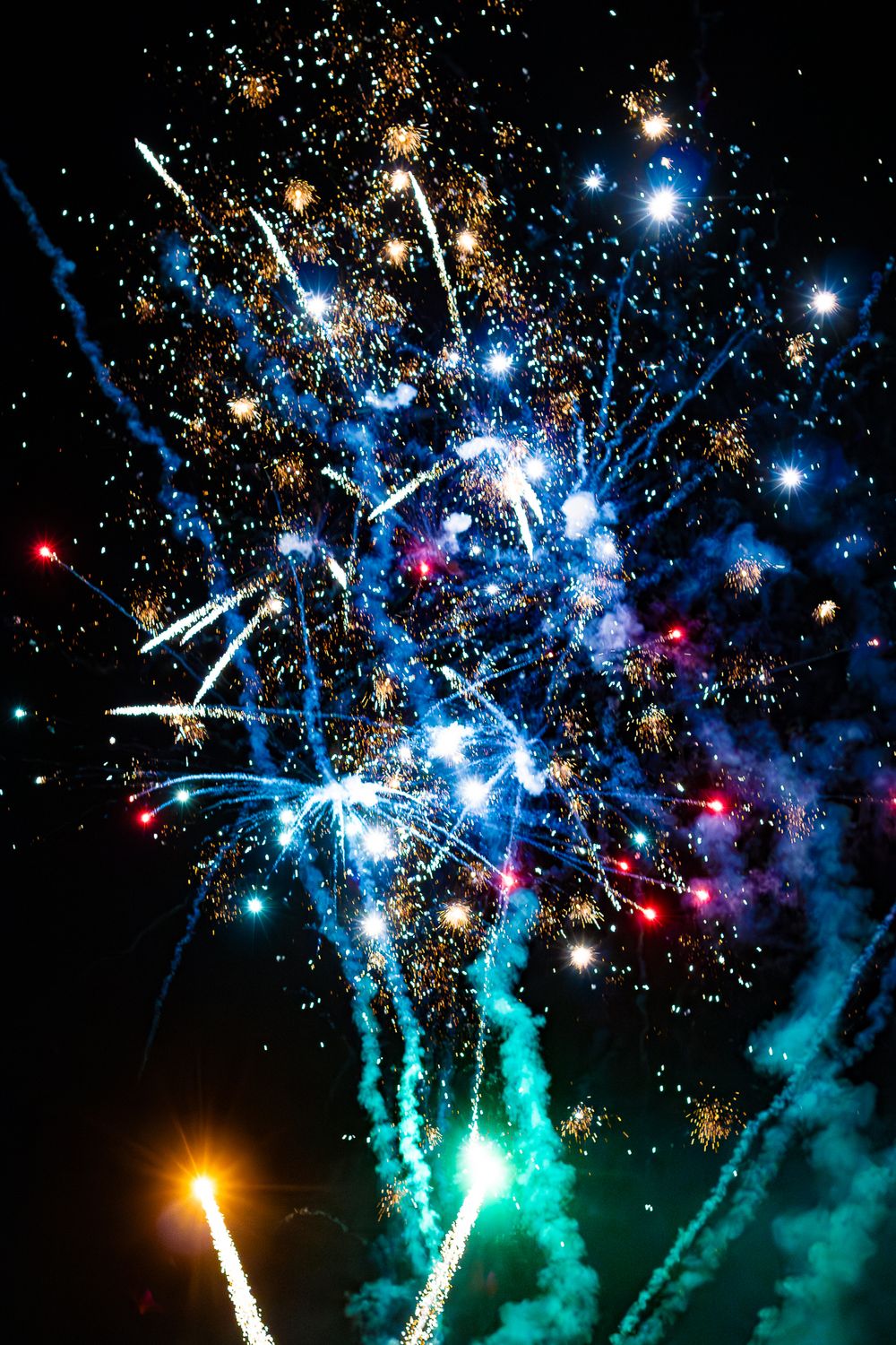 Colorful fireworks display with blue, gold, and red bursts lighting up the night sky.