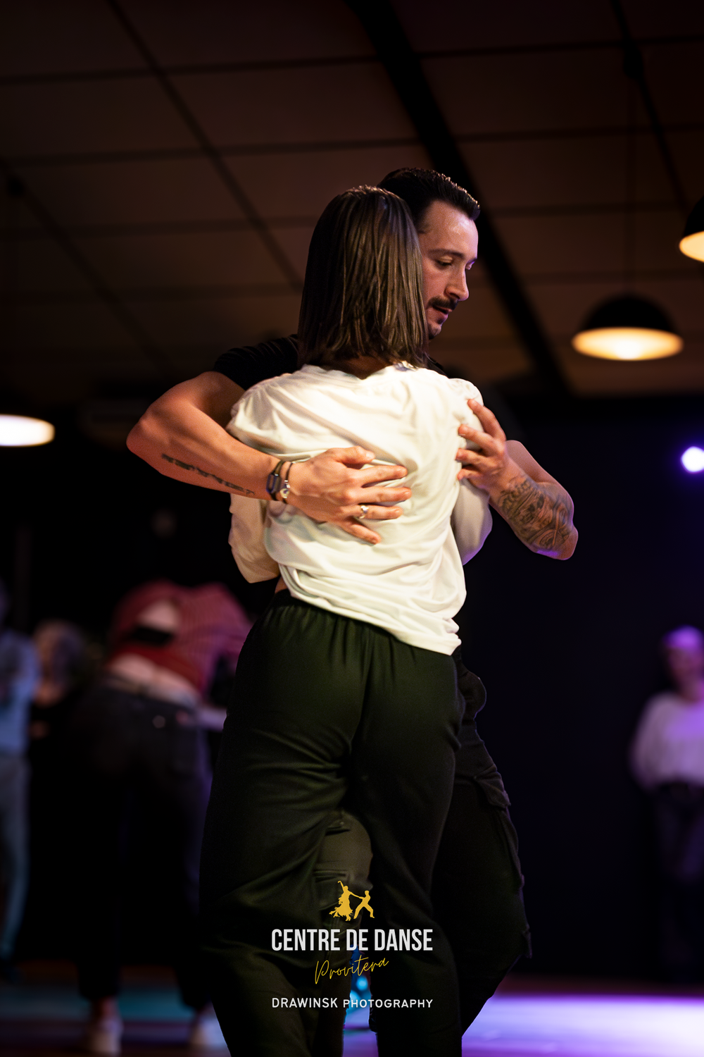 Two dancers embrace closely on a dimly lit dance floor at Centre de Danse, performing an intimate partner dance.