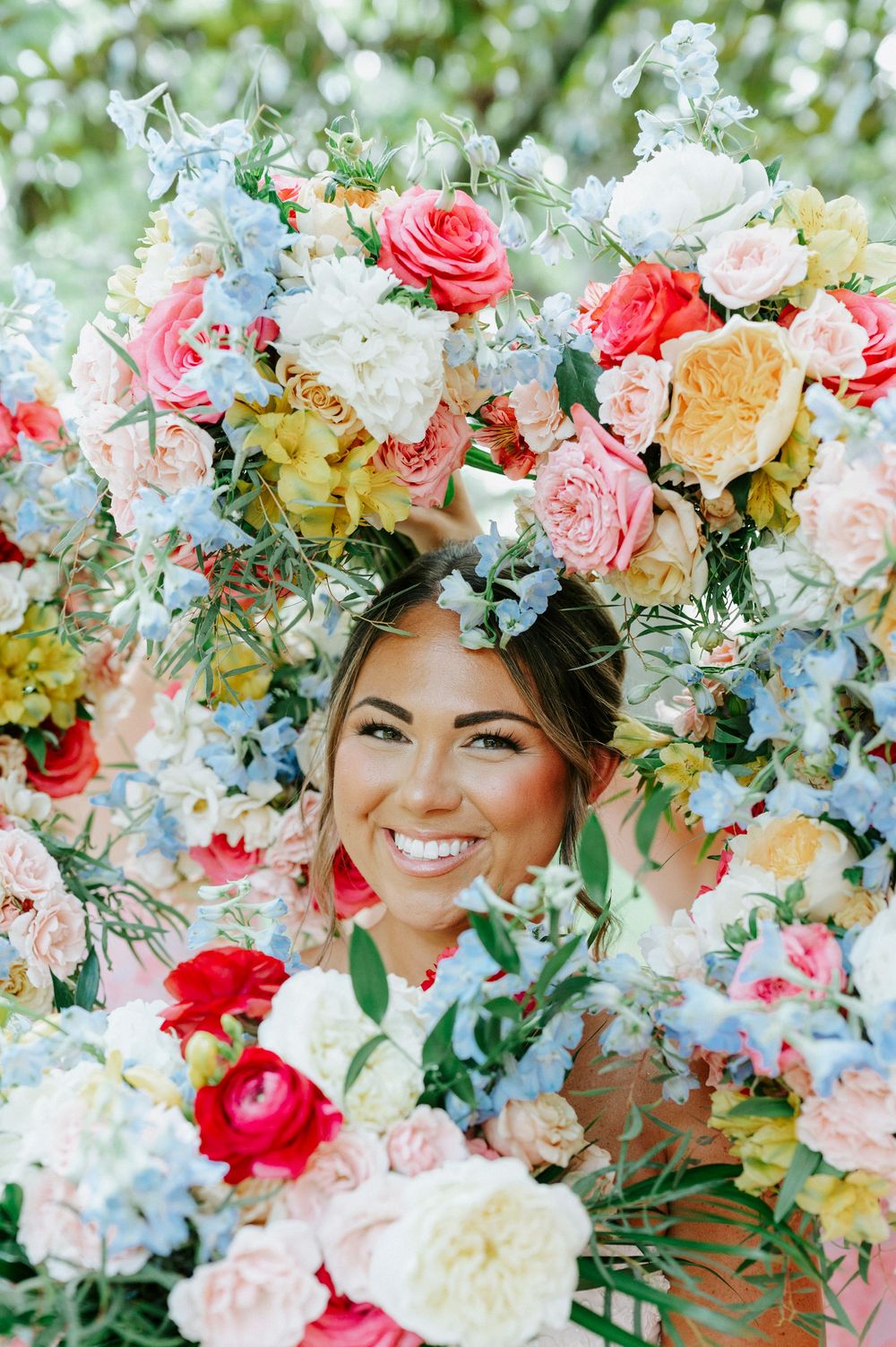 Smiling bride surrounded by vibrant colorful wedding bouquet of pink, blue, and white flowers.