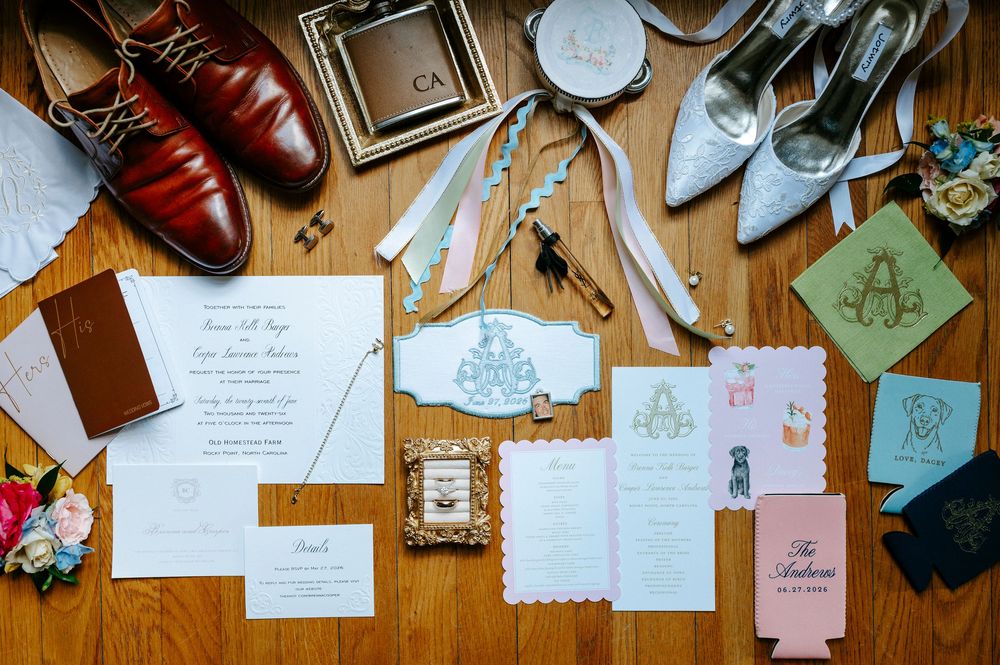 Flat lay of wedding stationery, invitations, shoes, and accessories arranged on wooden floor.