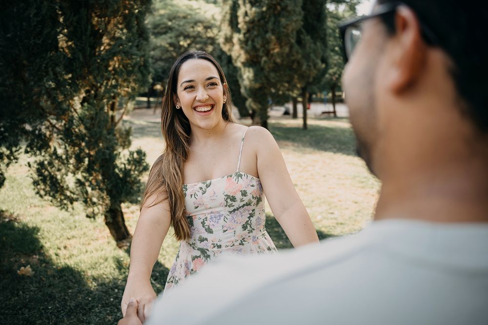 Smiling woman in floral dress holding hands with partner in sunny park.