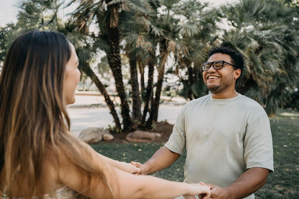 Happy couple holding hands and smiling outdoors near palm trees in a park.