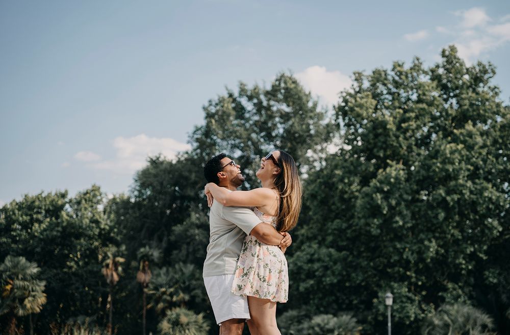 A joyful couple hugging and gazing at each other outdoors with lush green trees in the background.