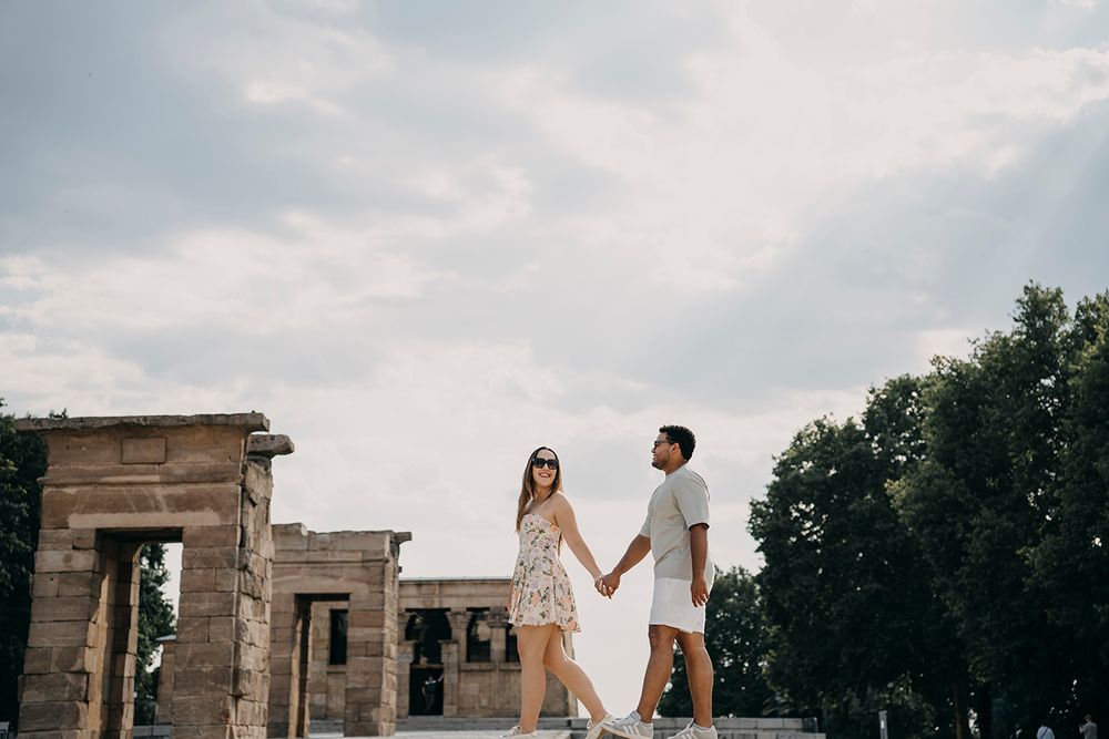 Couple holding hands walking at the ancient Temple of Debod ruins in Madrid on a cloudy day.