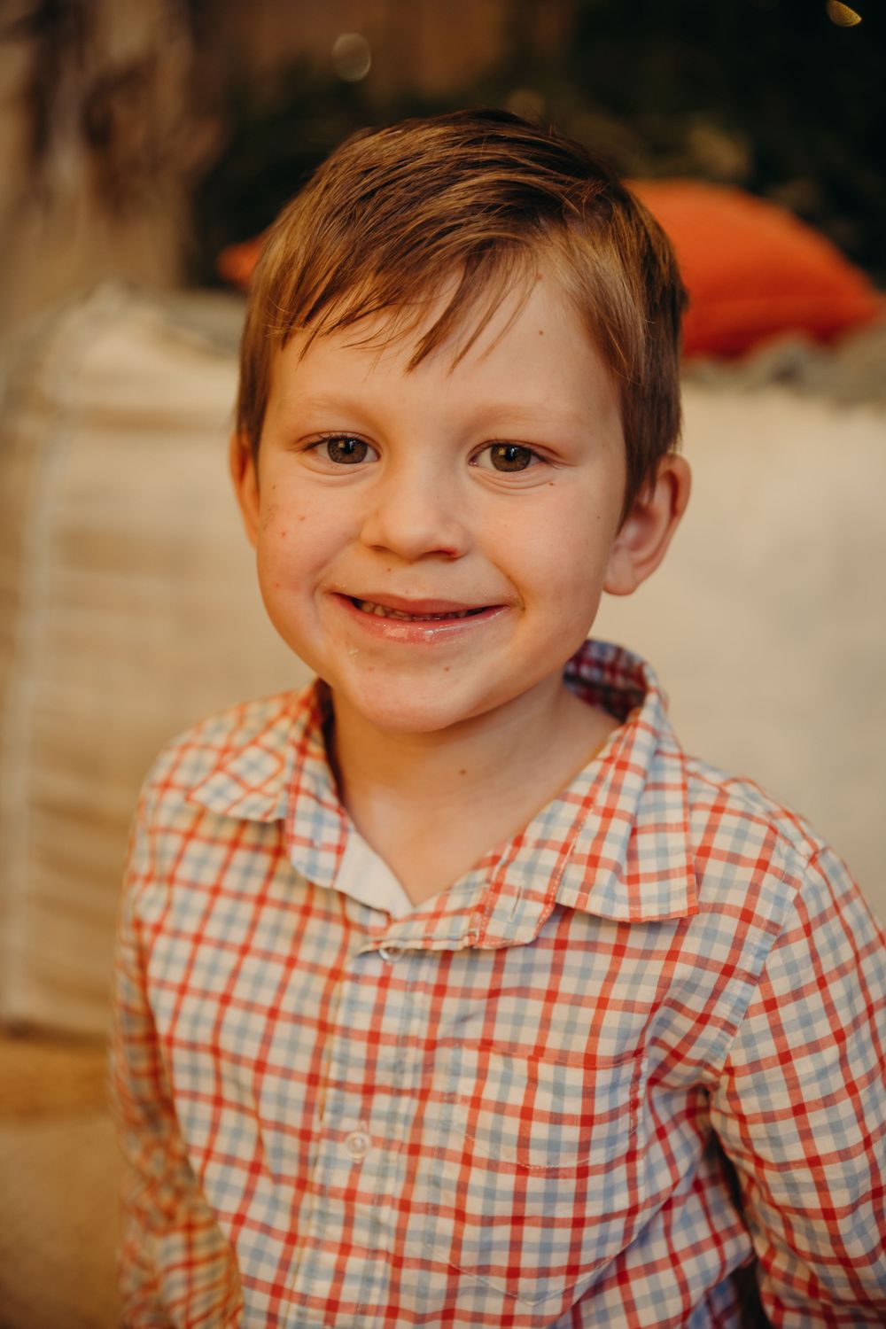Smiling young boy in a plaid shirt posing for a portrait in a warmly lit room.