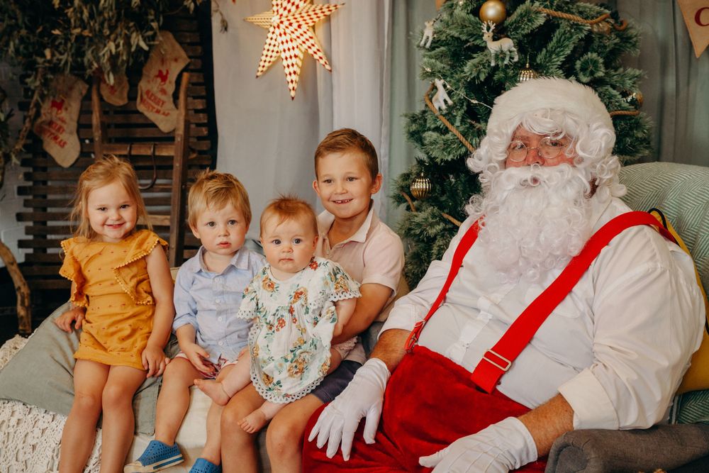 Four young children sitting with Santa Claus in a cozy Christmas decorated studio setting.