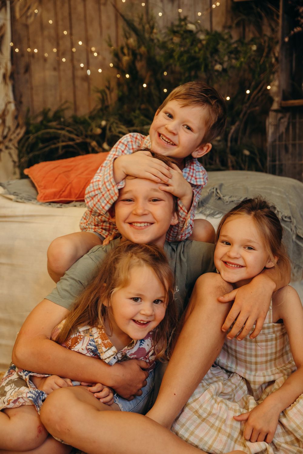 Four happy children hugging and laughing together in a warmly lit rustic decorated room.
