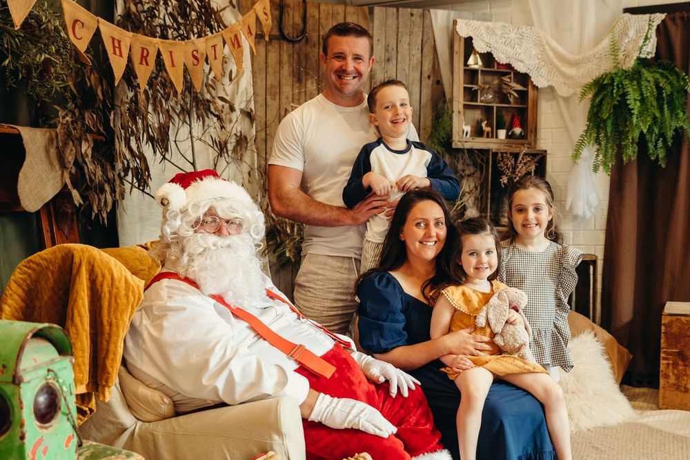 Family posing with Santa Claus for a festive Christmas photo session in a decorated Australian bush setting. Kristielle Gibbons Photography