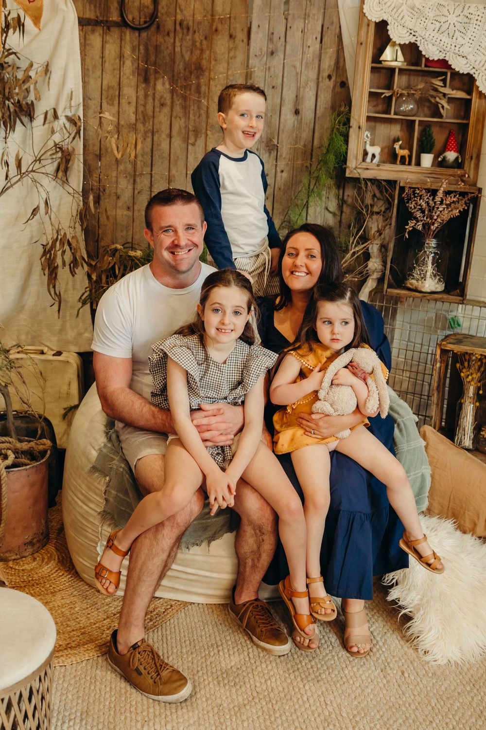 Happy family of five with three children posing in rustic boho styled indoor photography studio setting.