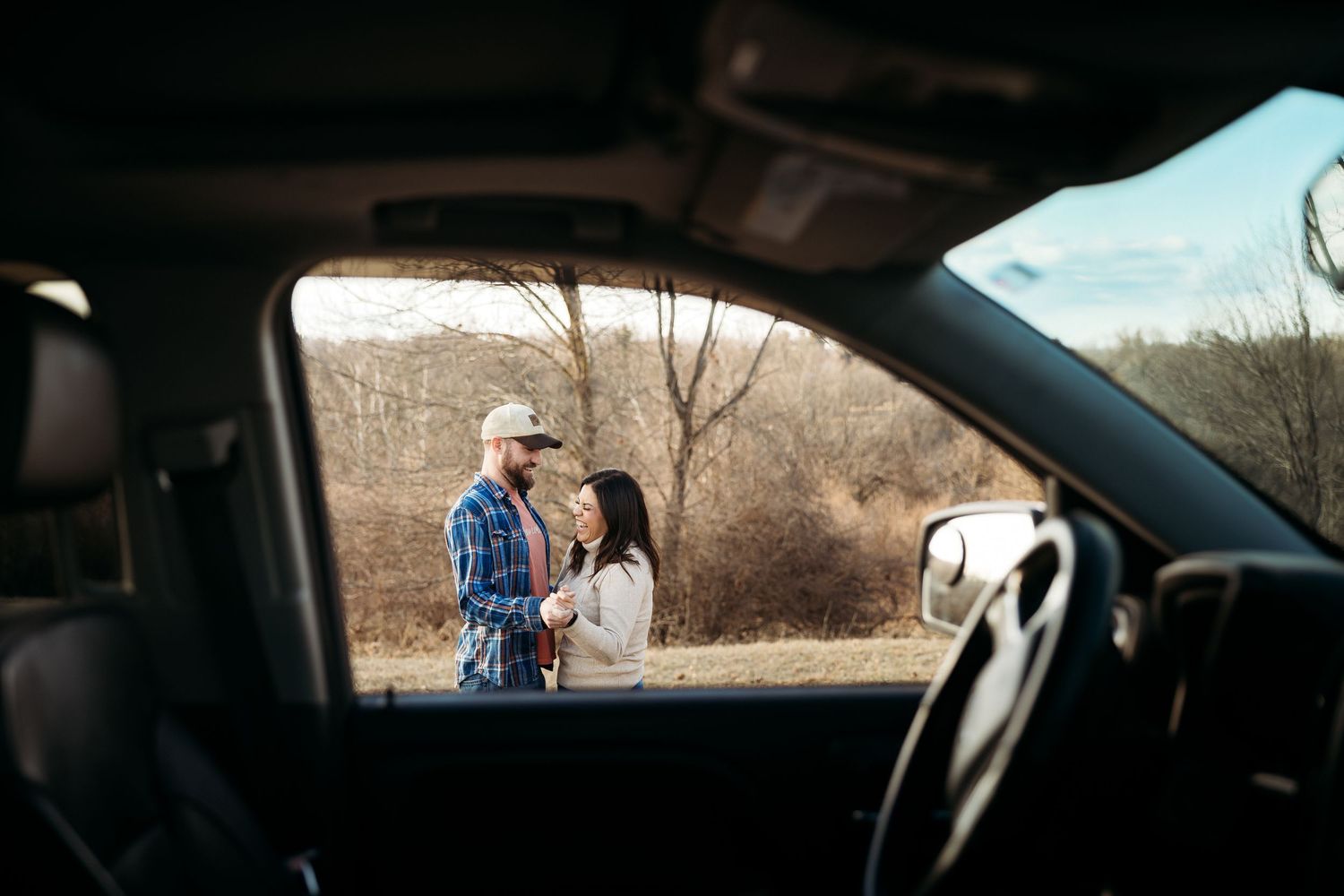 A couple shares a romantic moment on a motorcycle on a rooftop parking lot with a city skyline in the background.