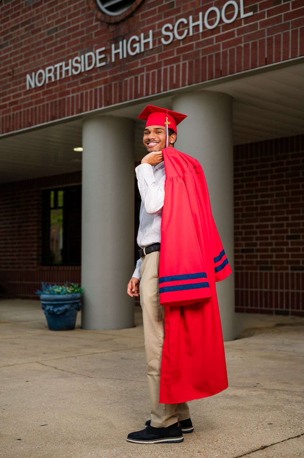 A proud high school graduate poses in a red cap and gown outside Northside High School.