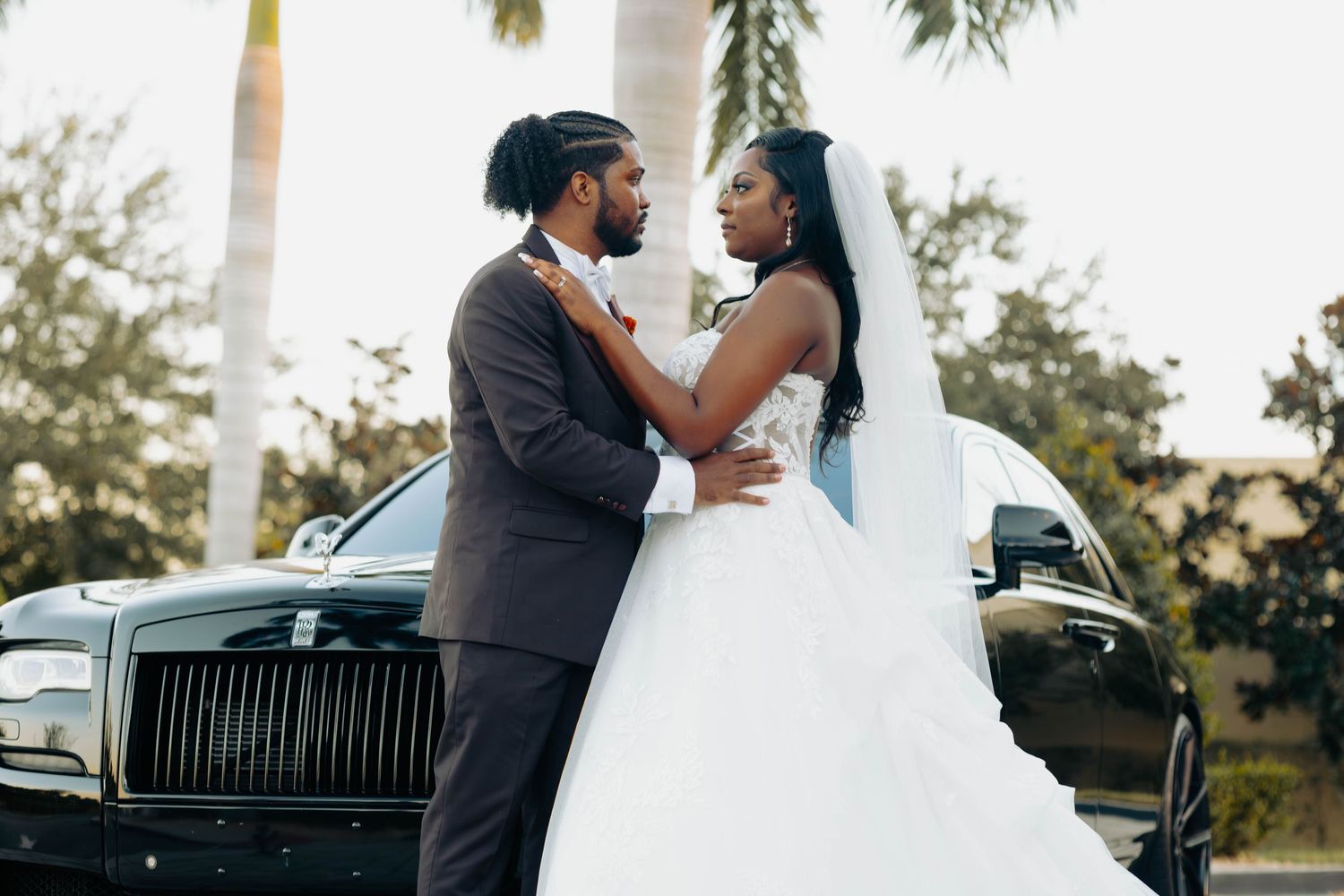 Bride and groom share a romantic moment in front of a Rolls-Royce, with the bride in a white ballgown.