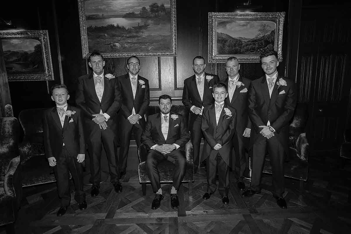 Black and white wedding photo of groom seated with groomsmen standing behind in elegant suits with boutonnieres.