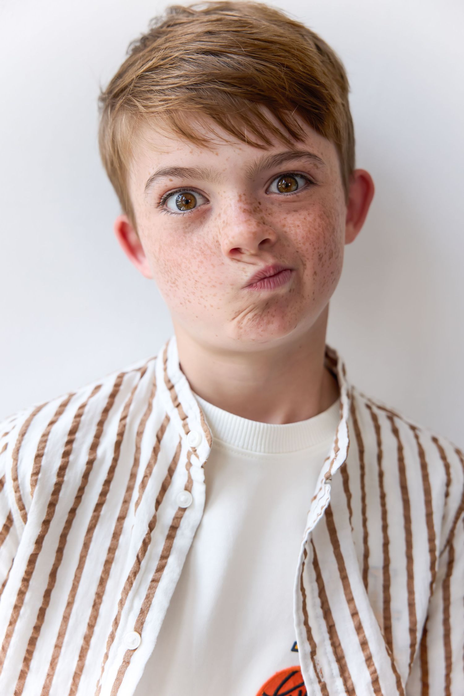 Portrait of a freckled boy with short hair making a funny face, wearing a striped shirt.