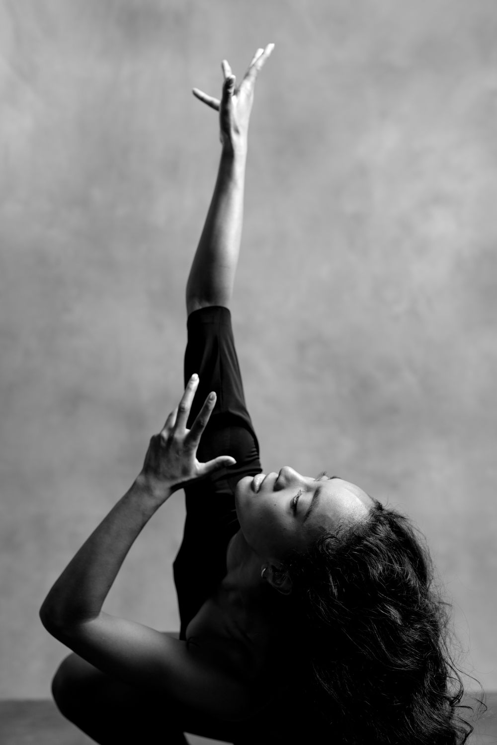 Black and white photo of a dancer reaching one arm upward gracefully while leaning back in an expressive pose.