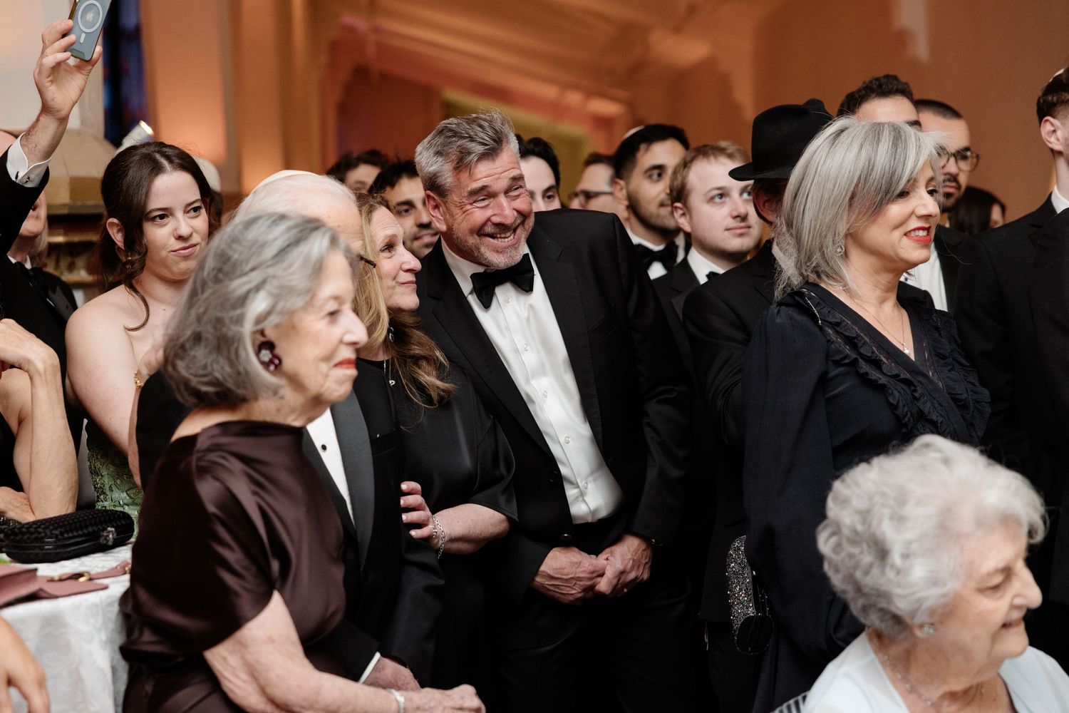 Elegantly dressed guests smile and mingle at a formal black-tie gala event in a grand venue.