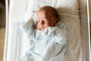 Newborn baby sleeping peacefully in hospital bassinet, wrapped in light blue swaddle blanket.