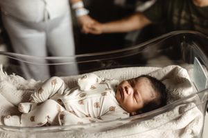 Newborn baby sleeping peacefully in a hospital bassinet wearing a white patterned onesie.