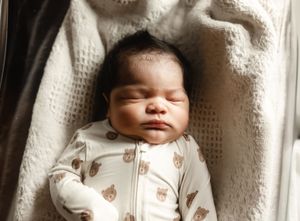 Newborn baby sleeping in a basket wearing a white bear-print zip-up sleeper.