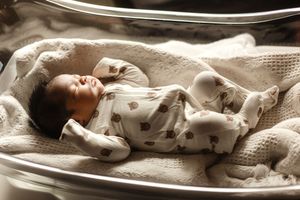 Newborn baby sleeping peacefully in a hospital bassinet, wrapped in a white patterned blanket.