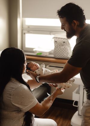 New parents tenderly hold their newborn baby together in a softly lit hospital room.