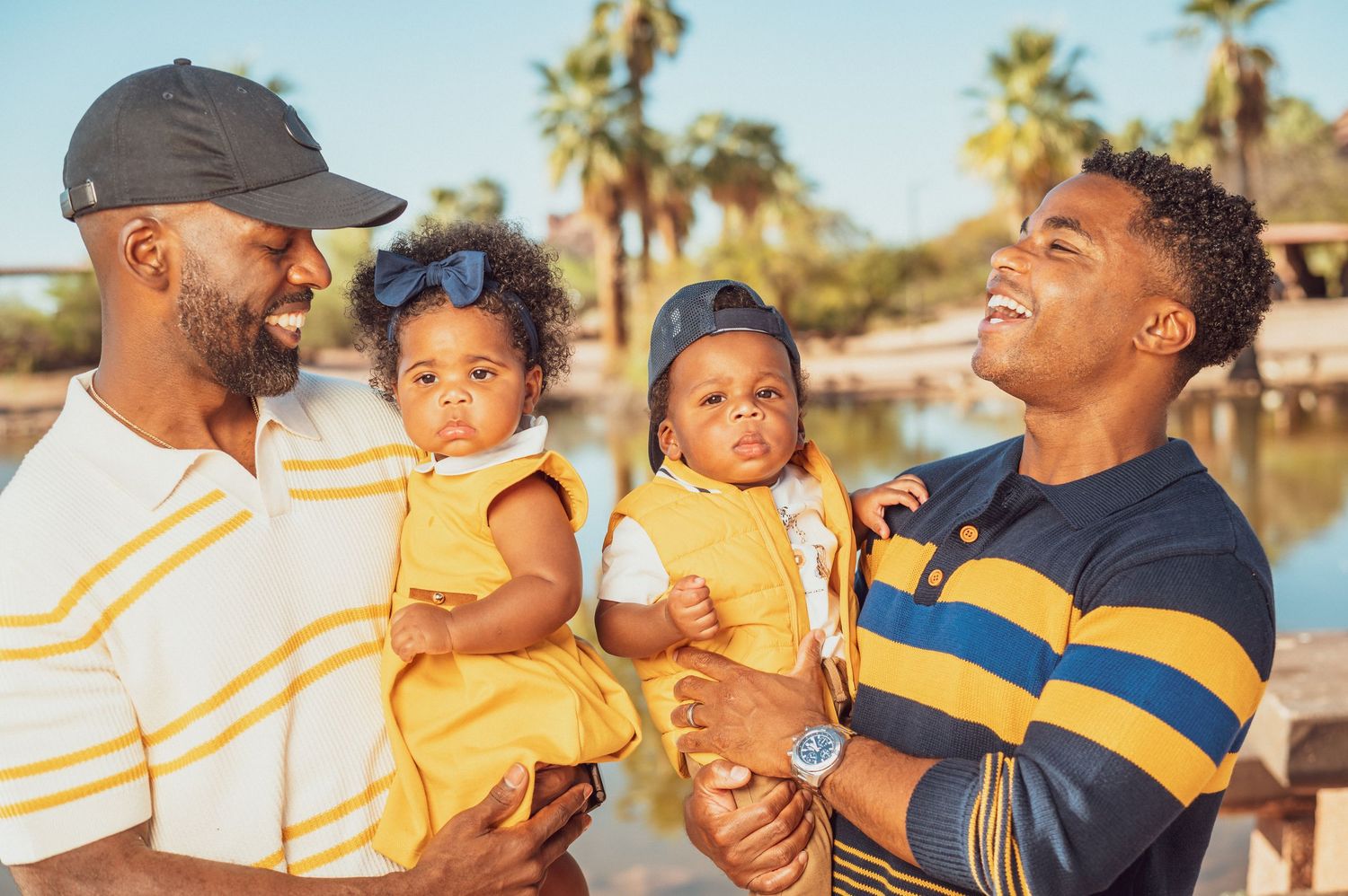 A smiling father holds his happy young daughter outdoors near a lake in a warm family portrait.