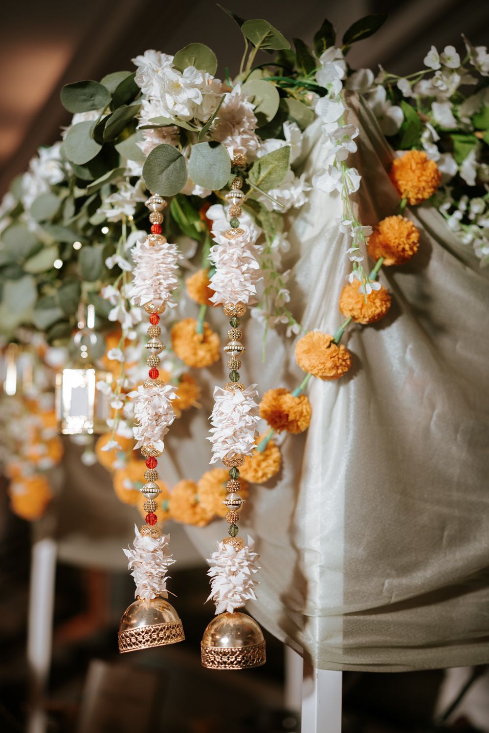 Traditional Indian wedding decor with marigold garlands, white flowers, and golden bell hangings on a mandap.