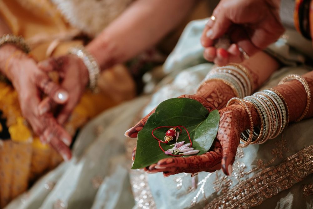 Bride's henna-adorned hands holding a green leaf with rings during an Indian wedding ceremony.