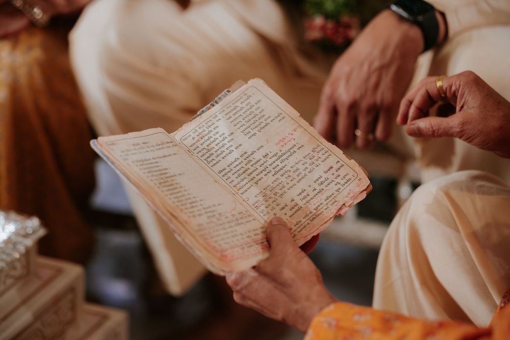 Hands holding an ancient religious text during a traditional ceremony, with people in white garments in the background.