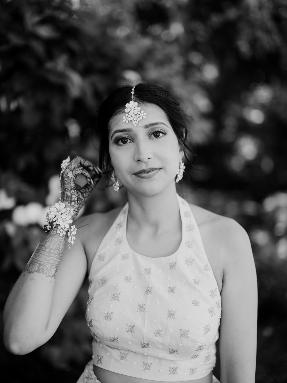 Black and white portrait of Indian bride wearing maang tikka and mehndi with floral wrist accessory.