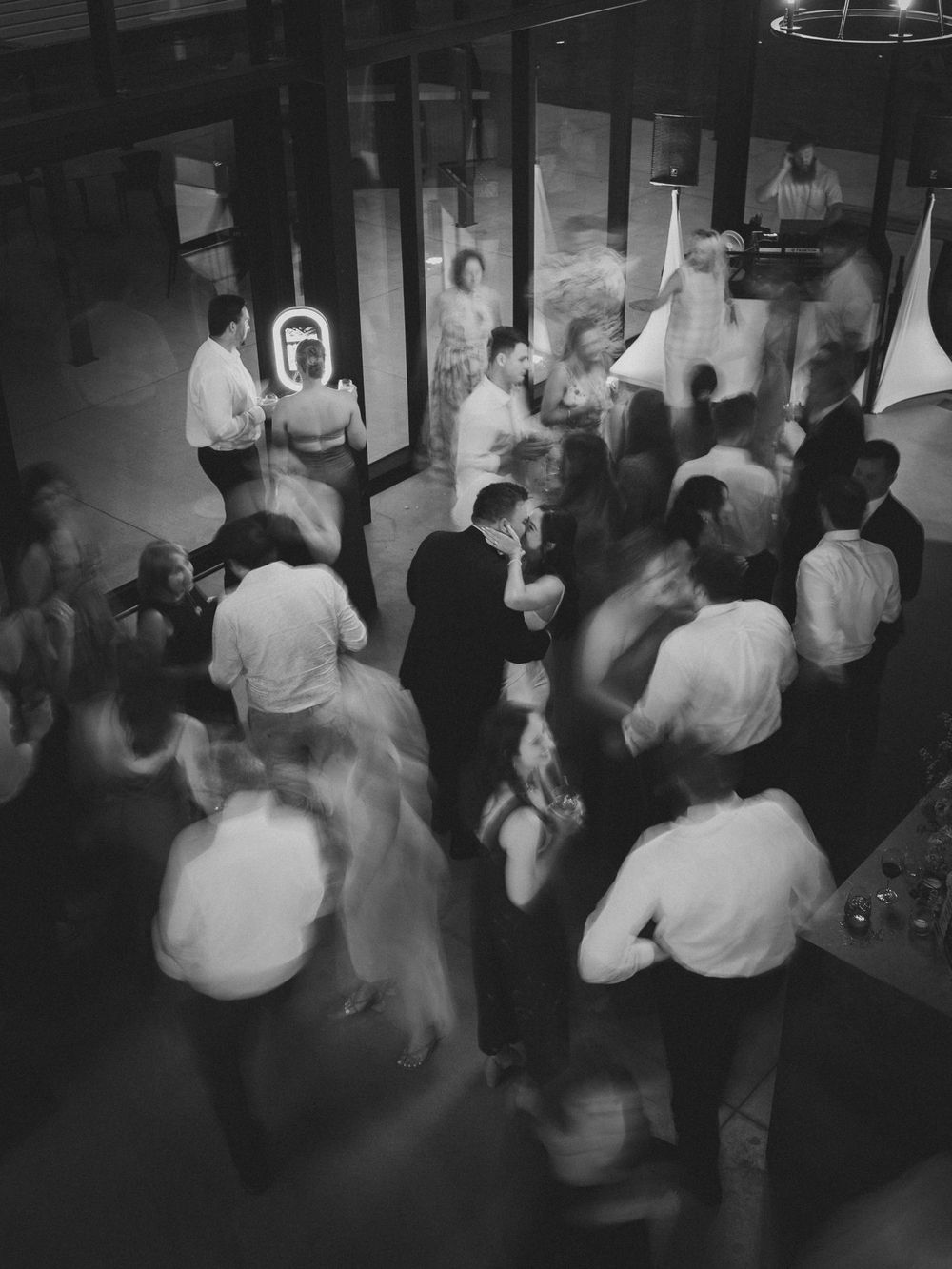 Black and white aerial view of wedding guests dancing at a lively indoor reception party.