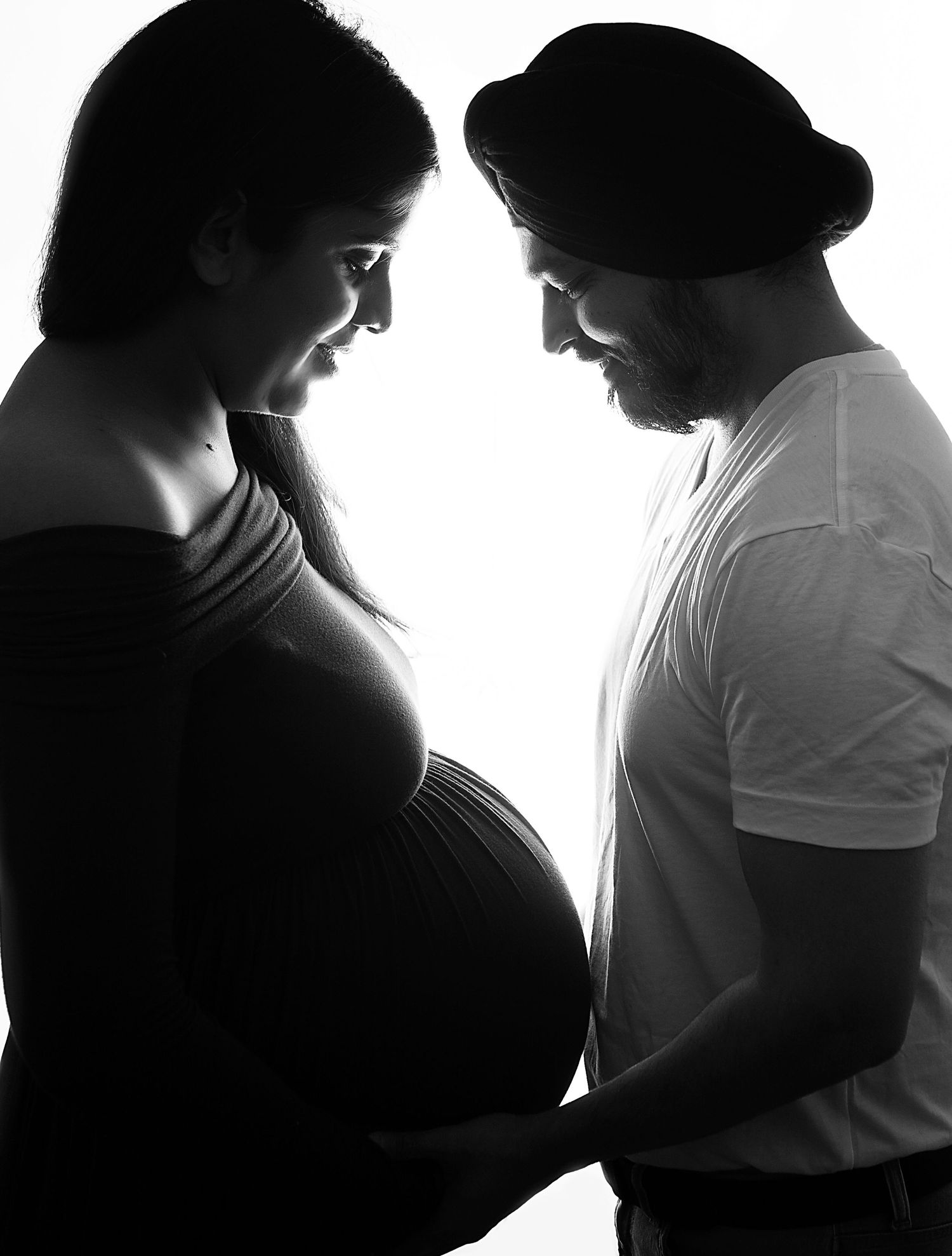 Black and white maternity photo of pregnant woman and man in hat facing each other in silhouette. during a maternity photoshoot in Bexley