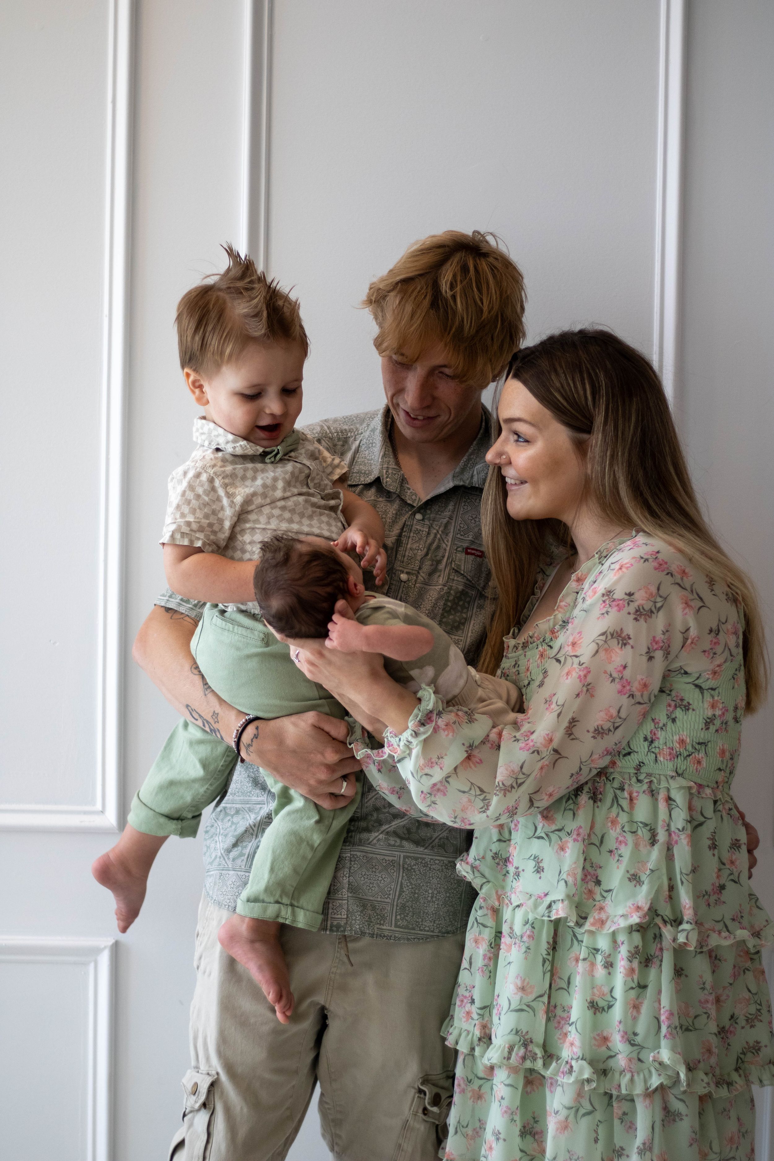 Happy young family with two small children posing together in a bright white room, parents smiling lovingly at their babies.