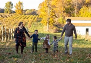Family of five holding hands walking through a vineyard in autumn foliage on a sunny fall day.