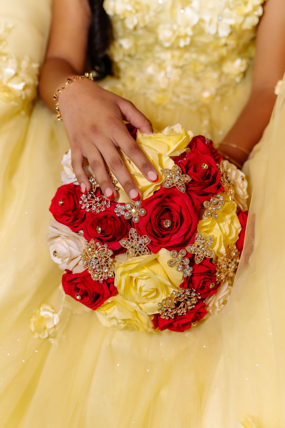 Young woman in yellow gown holding red, yellow, and white rose bouquet with gold brooch accents.