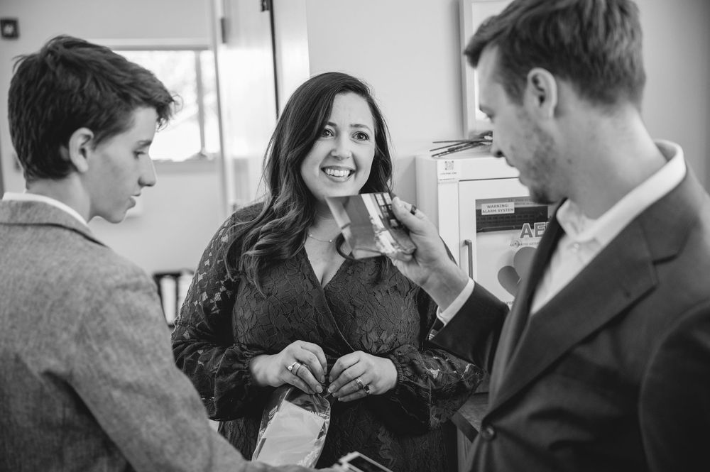 Black and white photo of a smiling woman chatting with two men at a social gathering.