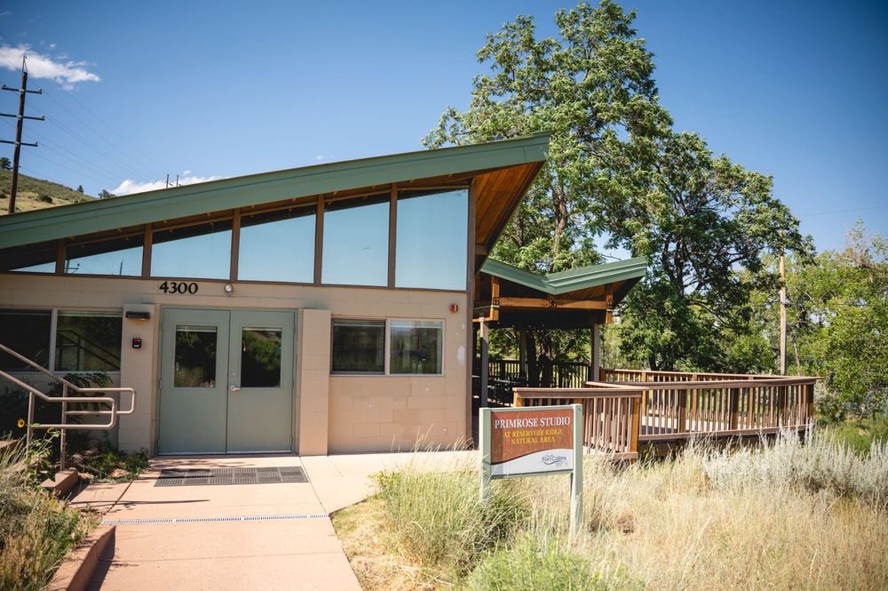 Rustic visitor center building with wooden deck, surrounded by lush trees and natural landscaping in a mountain setting.