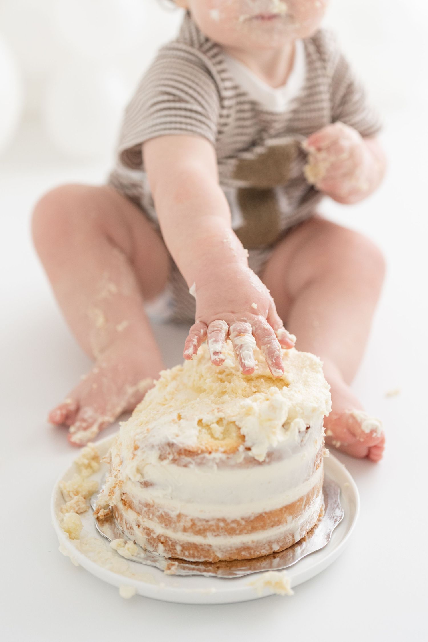 Plan rapproché sur les doigts de bébé qui explorent le crémage de son gâteau lors de sa séance premier anniversaire au studio