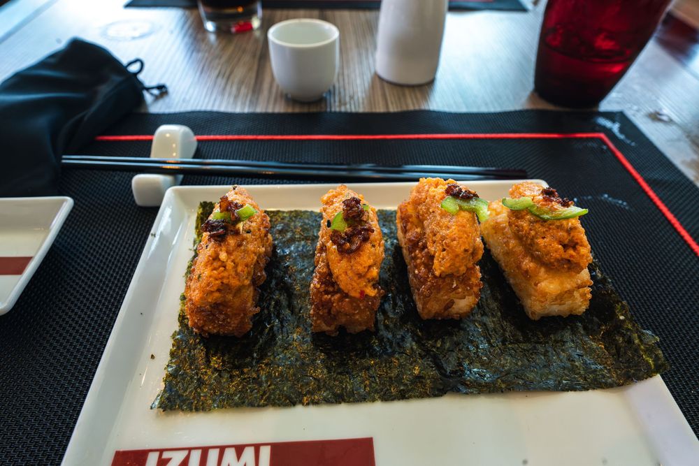 Four pieces of crispy baked sushi rolls on nori at Izumi restaurant, served with chopsticks on a white plate.