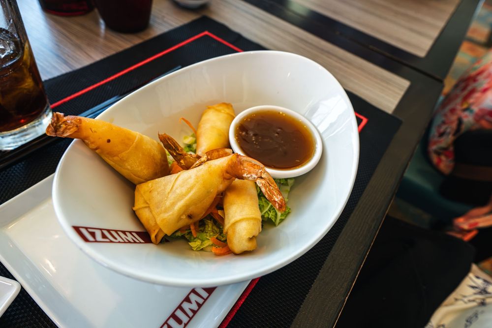 Golden fried spring rolls with dipping sauce served in a white bowl at Izumi restaurant.