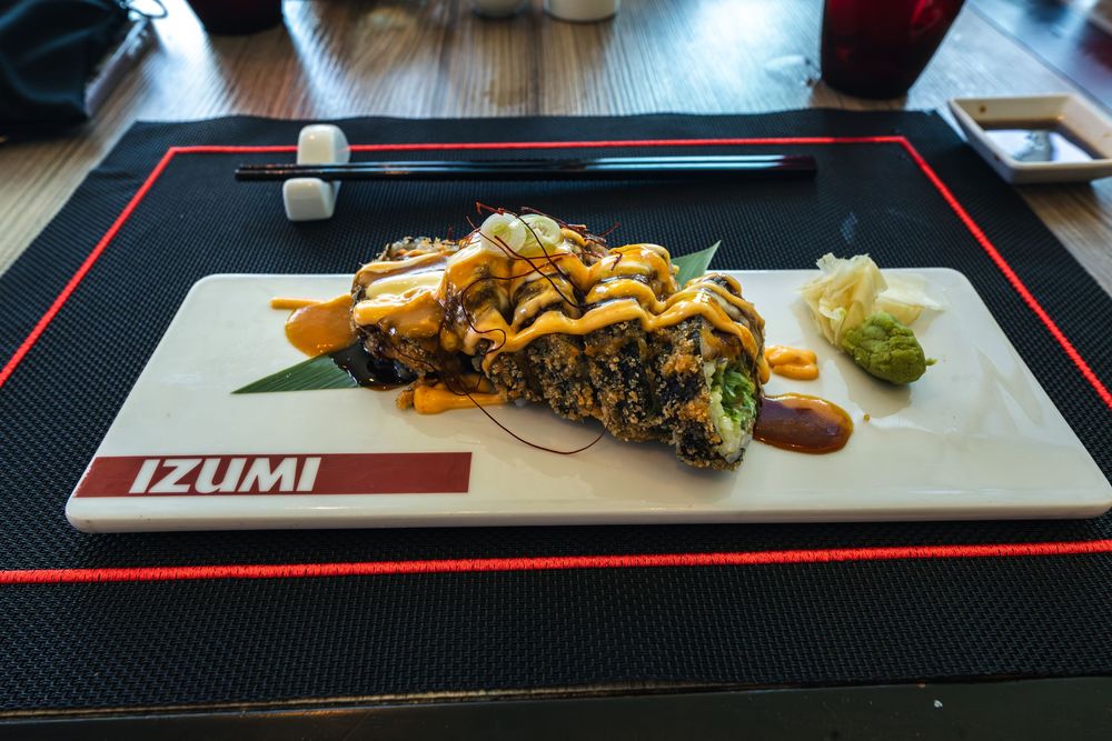 Izumi restaurant sushi roll platter with drizzled sauce, wasabi, and ginger on a white ceramic plate.