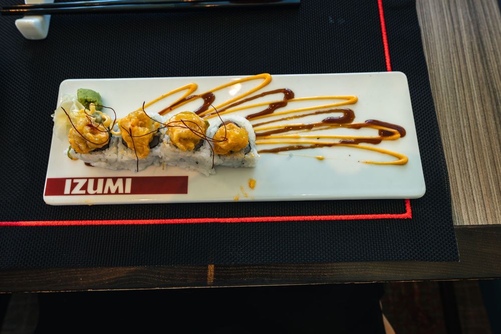 Izumi restaurant sushi rolls with orange tobiko and drizzled teriyaki sauce on a white rectangular plate.