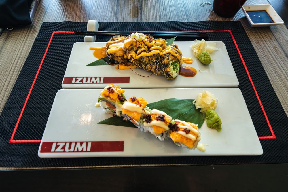 Two plates of elaborately garnished sushi rolls served on white Izumi restaurant platters with wasabi and ginger.